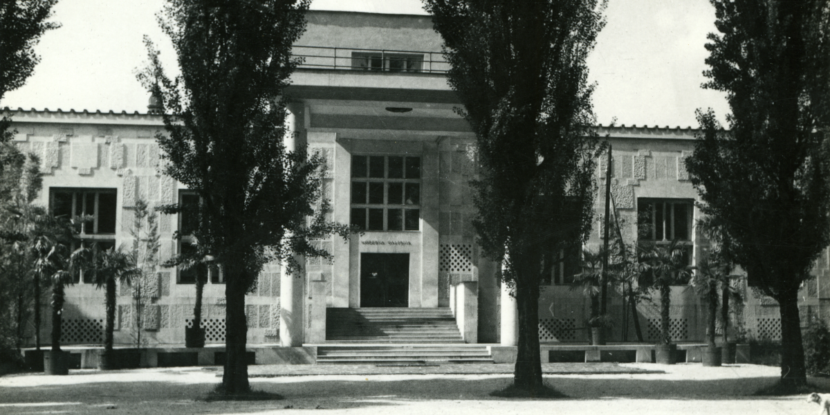 Pročelje z vhodom v Moderno galerijo. Pred pročeljem so tri visoka drevesa. Tik ob stavbi se nahaja še nekaj manjših palm, ki rastejo v posodah. Črno-bela fotografija je nastala okrog leta 1950.